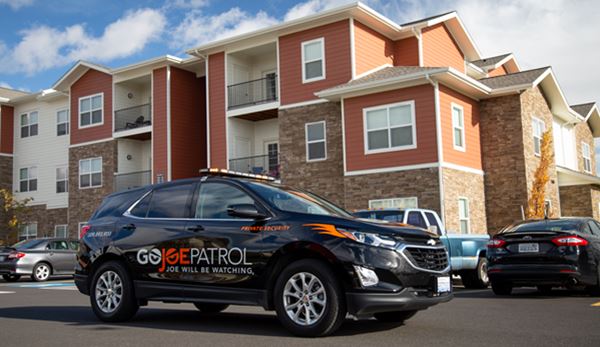 Photo of black GoJoe Patrol car parked in front of red apartment building.
